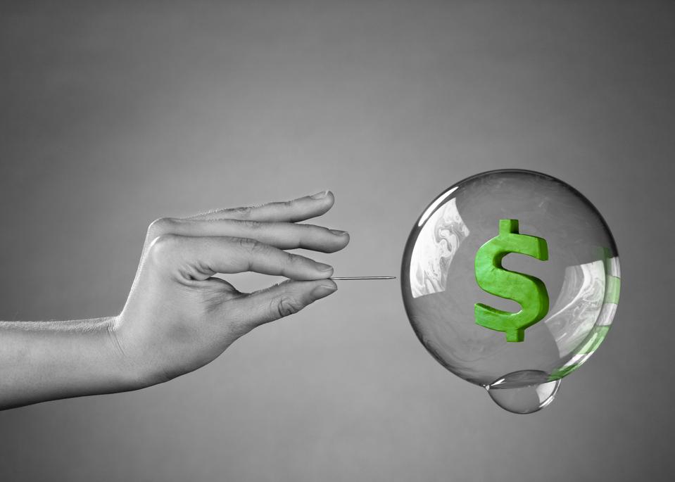 Hand holding needle about to pop bubble with dollar sign