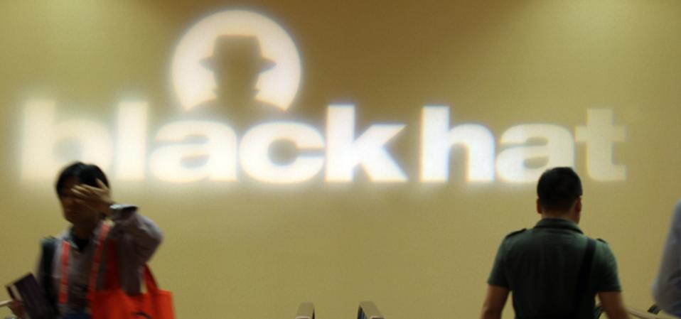 The Black Hat conference logo projected onto a wall above a bank of escalators.