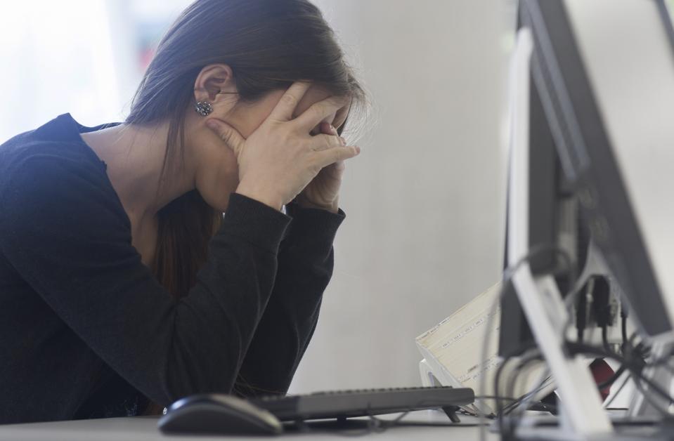 Side view of woman sitting at computer head in hands