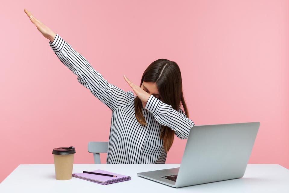 Extremely excited happy woman office worker showing dab dance gesture, performing internet meme of success, sitting at workplace with laptop.
