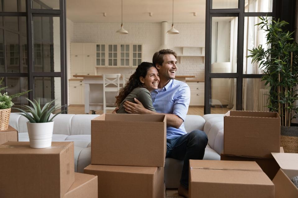 Happy millennial married couple hug on sofa at relocation day