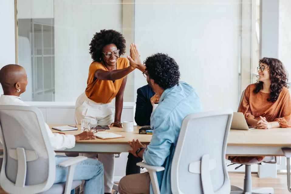 Marketing and sales teams collaborate productively, give a high-five in meeting.
