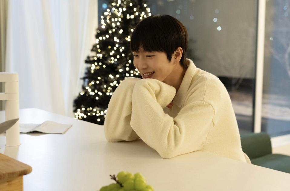 A smiling young man sits at a counter in front of a Christmas tree.
