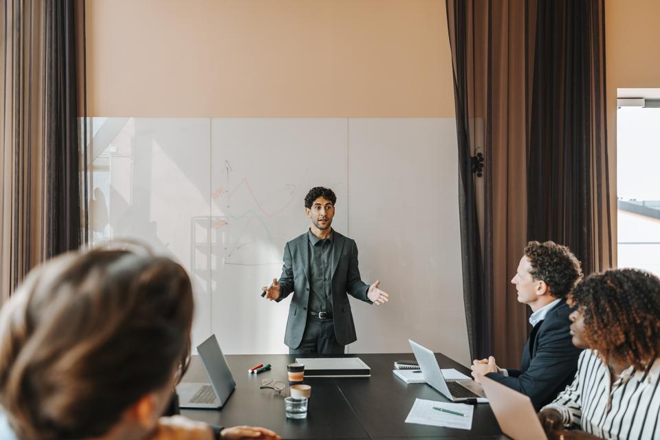 Young male entrepreneur explaining strategies to colleagues sitting in board room at office