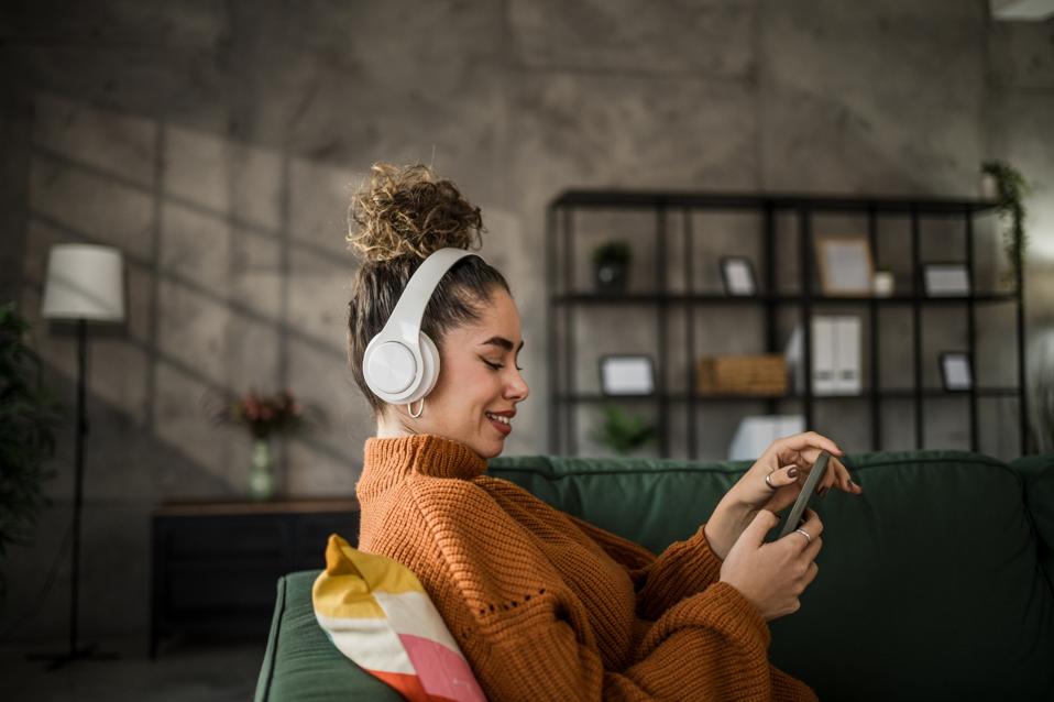 Excited young woman listening to music on wireless headphones over a mobile app while sitting on a comfortable sofa