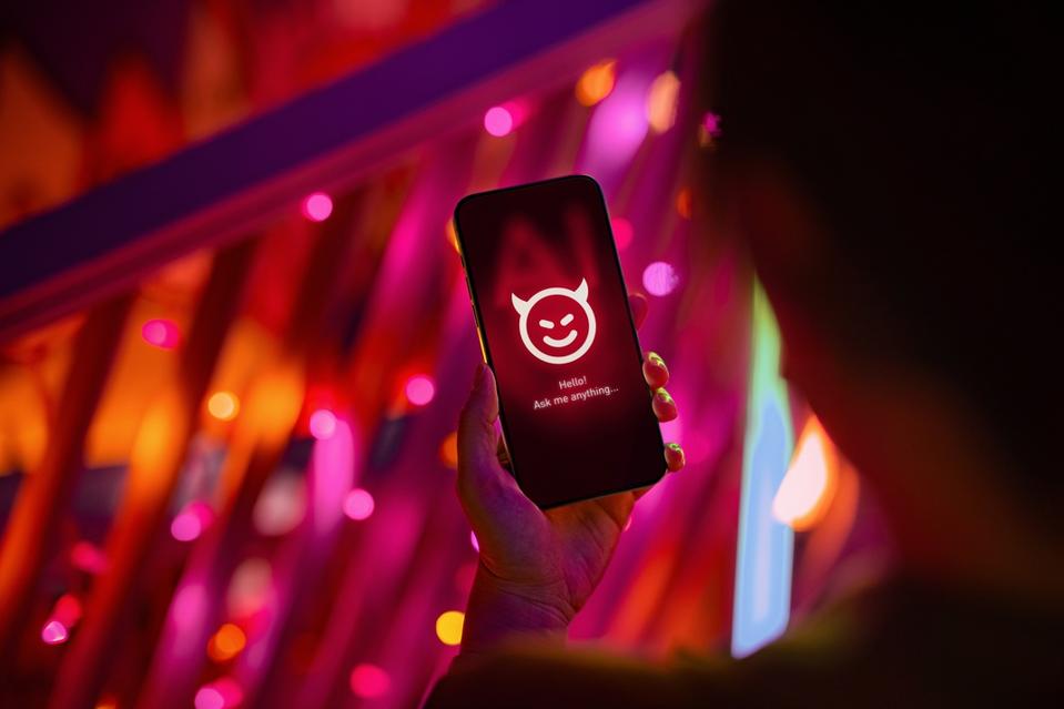 Female hand holding smartphone showing an evil with devil horn on her AI chatbot conversation app in the city. Illustrating the ideas around the risks and dangers of Artificial Intelligence (AI). The awareness and careful consideration of its implications