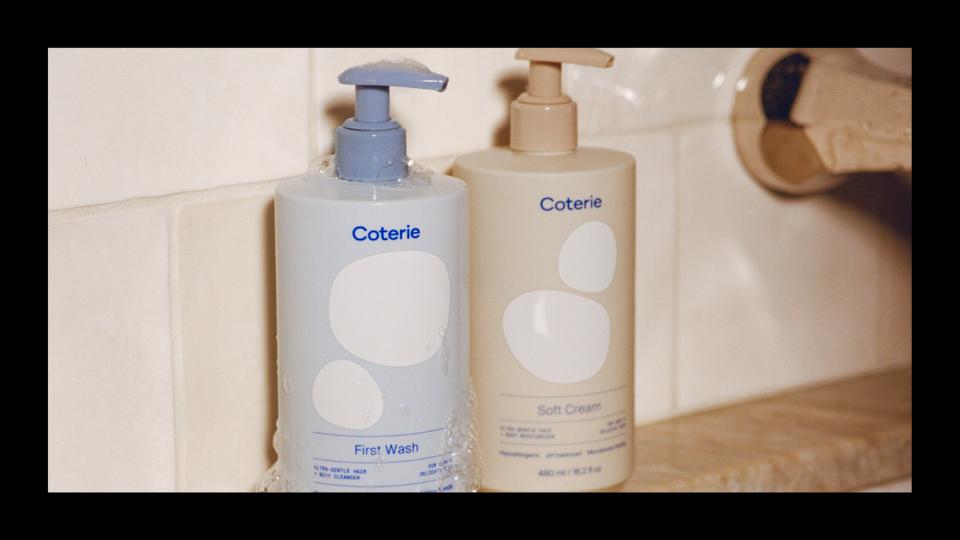 blue and tan bottles of Coterie skincare sitting on the edge of a bathtub
