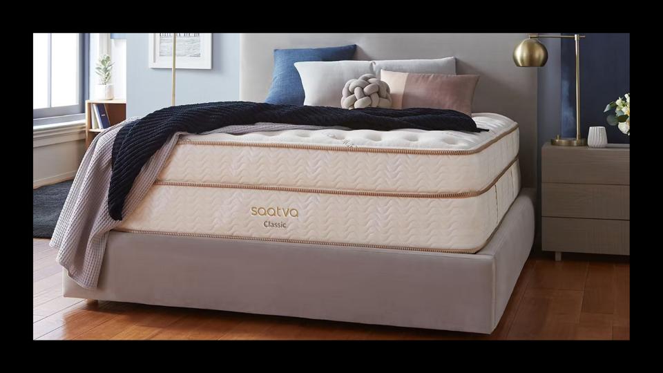 Saatva mattress in a bedroom with pillows and blankets on top