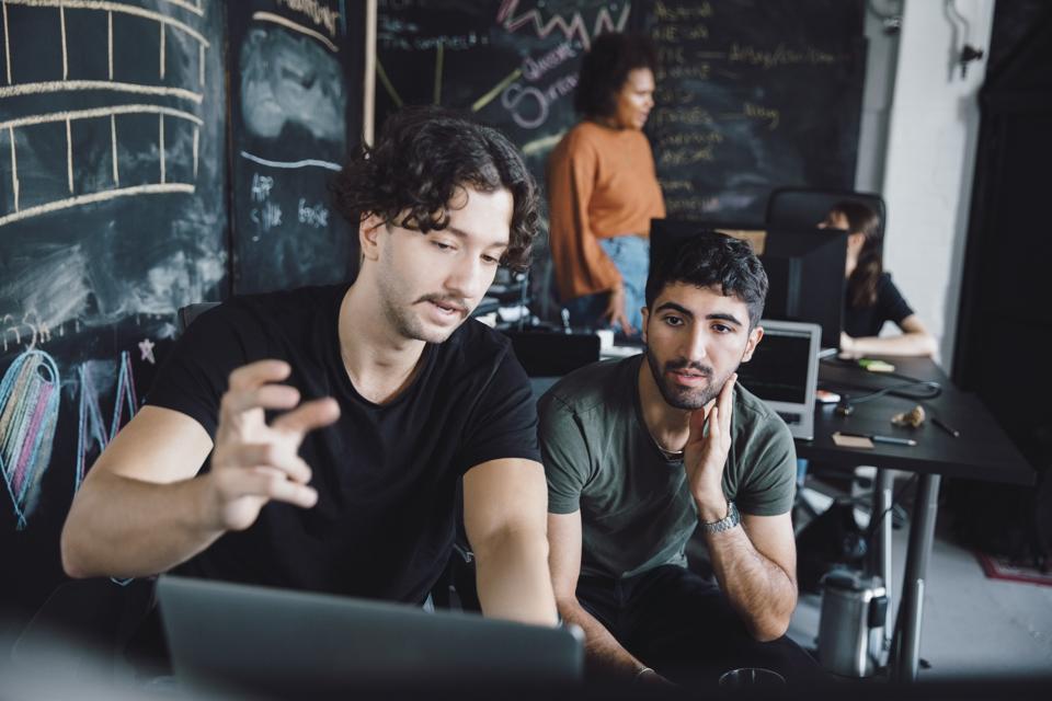 Two men looking at computer screen and two women nearby talking.