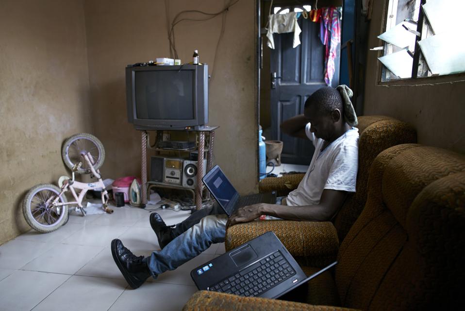 Man working on his laptop while sitting on a couch in a room with hanging laundry