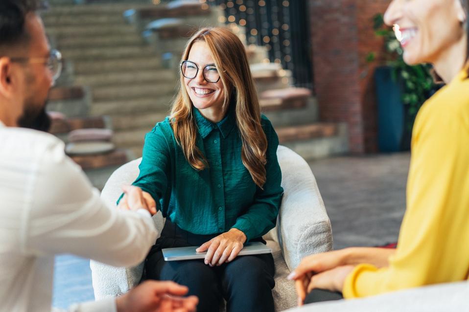 Jeune femme professionnelle avec ordinateur portable à genoux serrant la main d'un nouvel employeur.