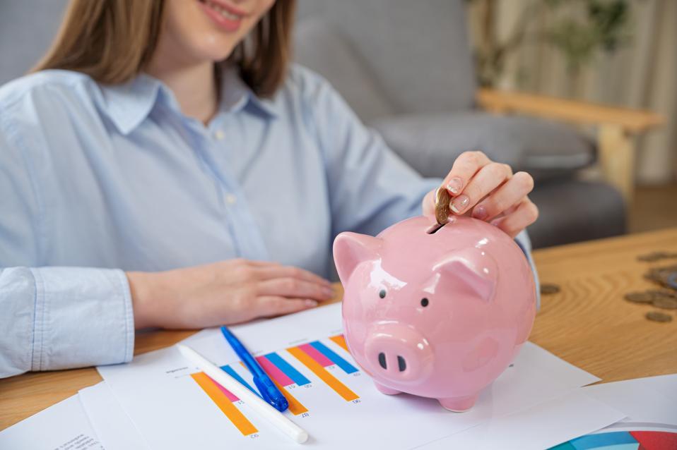 Woman hand putting money coin into piggy bank for saving money.