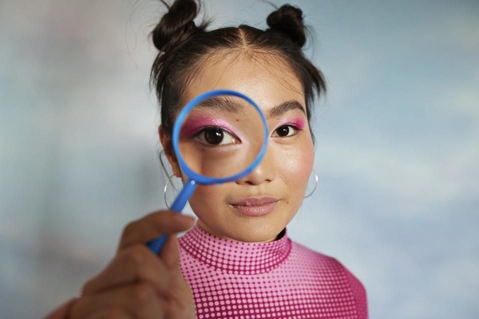Portrait of teenage girl looking through magnifying glass against colored background