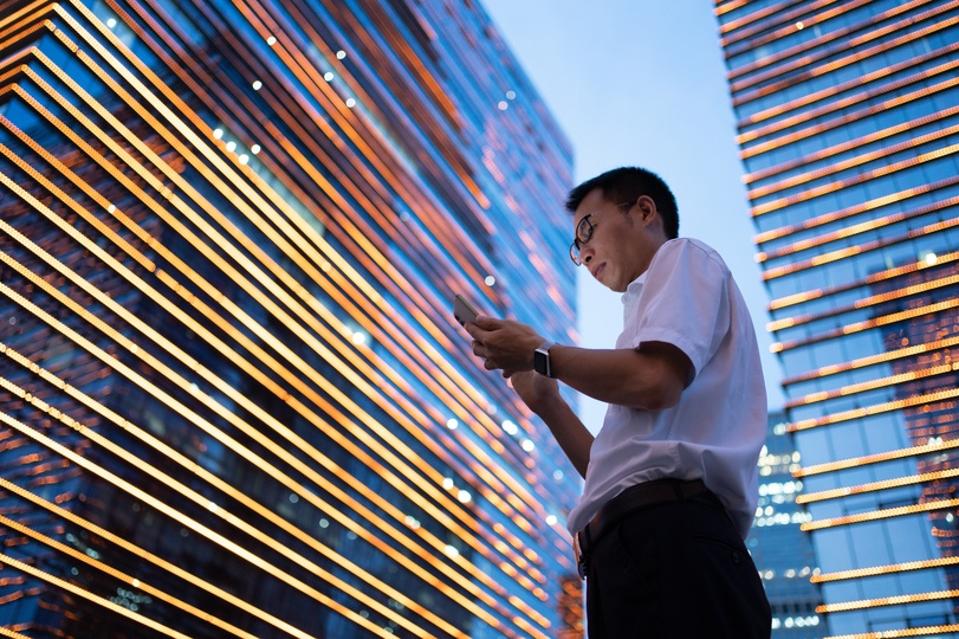 A young Asian businessman wearing a white shirt is using a smartphone