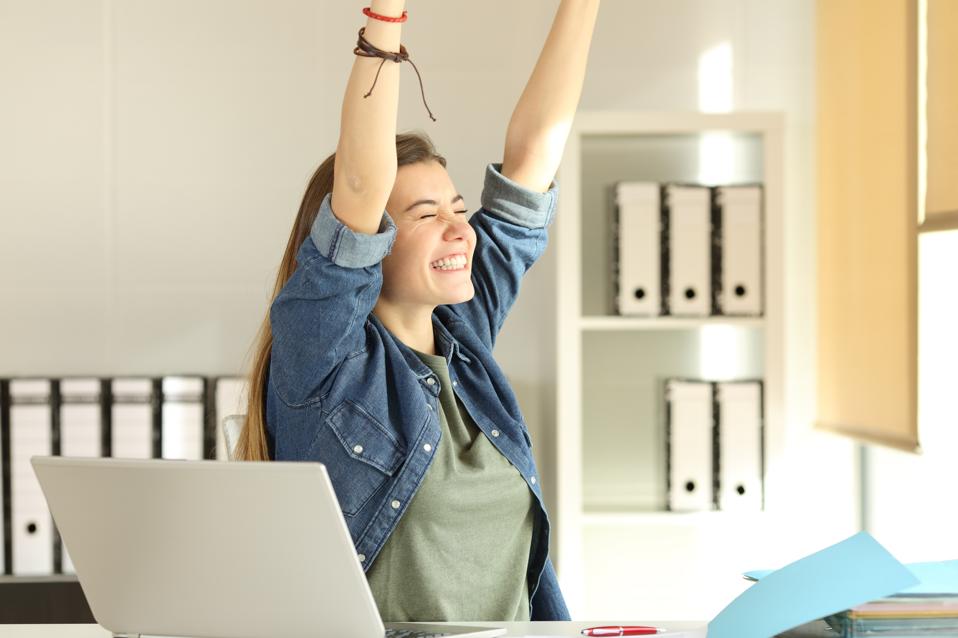 Motivated woman celebrating at desk, symbolizing The Great Lock In trend and career goals.