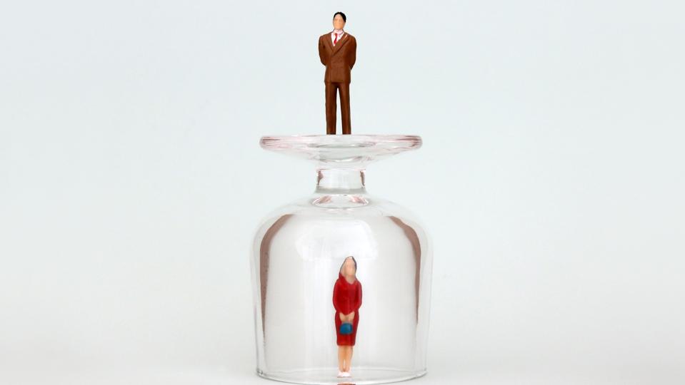 A miniature woman in a glass cup and a miniature man on top of a glass cup. The concept of the gender promotion gap.