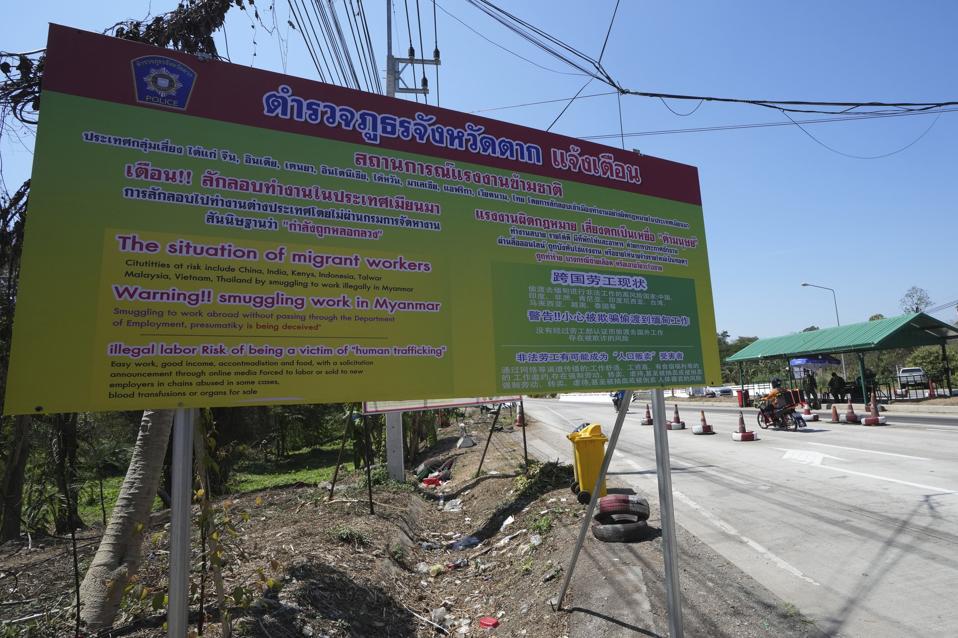 A roadside sign in multiple languages, mentioning "Warning!! smuggling work in Myanmar"