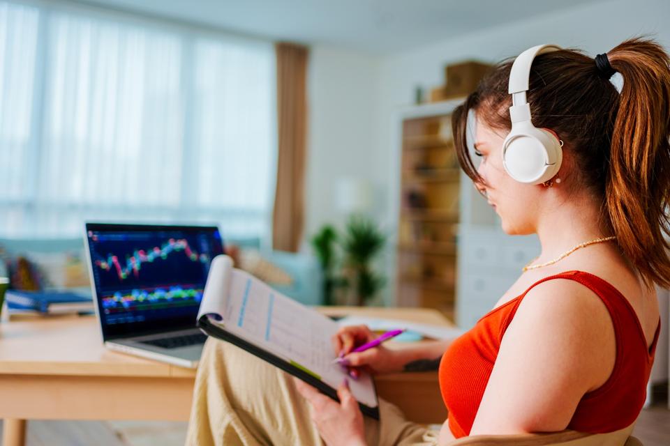 Young Businesswoman with Headphones checking Bitcoin or stock exchange price chart on digital exchange on a laptop monitor computer at her desk at home