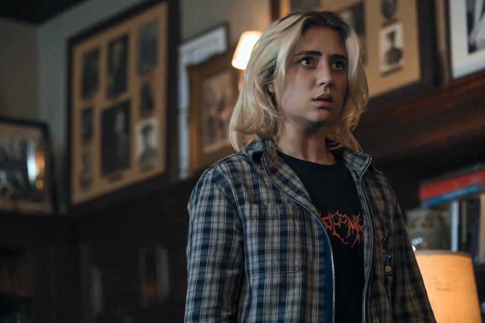 A woman with short blonde hair wearing a plaid shirt over a black T-shirt.