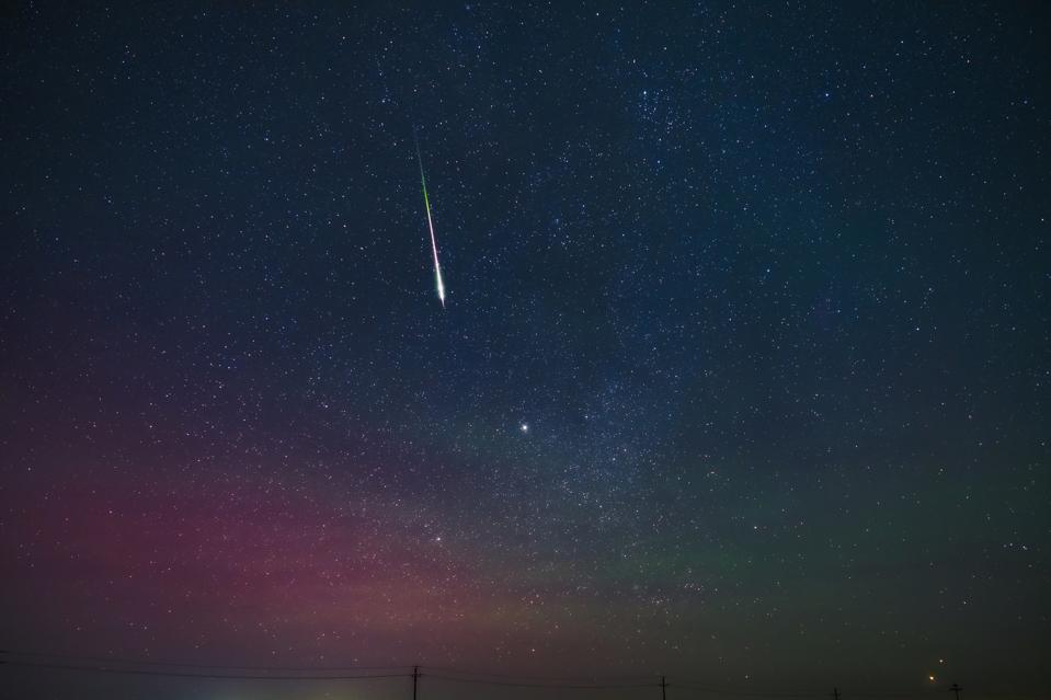 A fireball streaked across the sky above the wilderness accompanied by the aurora.