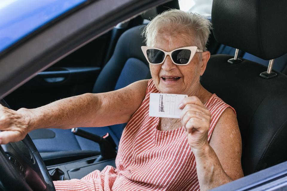 Feliz anciana de cabello blanco muestra su licencia de conducir sonriendo mientras comienza un viaje de vacaciones de verano conduciendo su automóvil