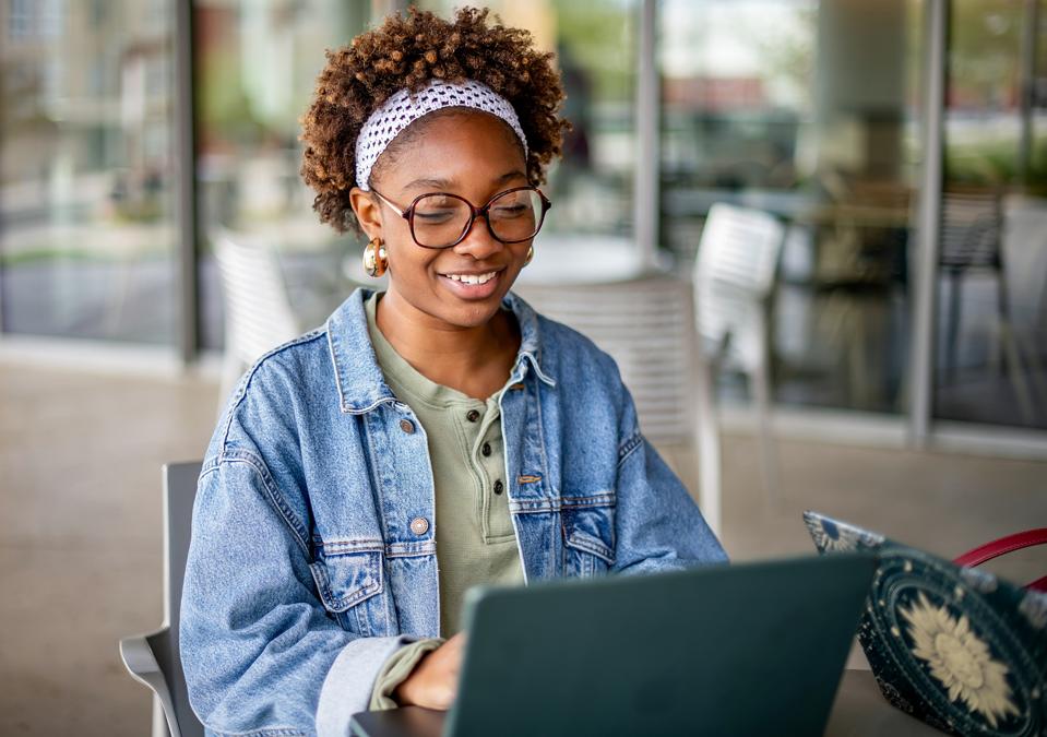 Young female college student smiling as she studies on her laptop in a campus setting