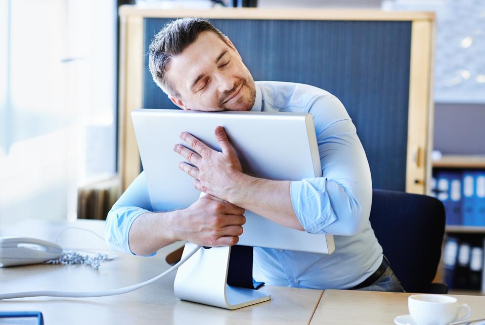 Businessman hugging a computer monitor, symbolizing the workplace trend known as job hugging.