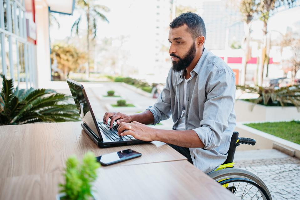 Homme de fauteuil roulant travaillant sur l'ordinateur à la cafétéria