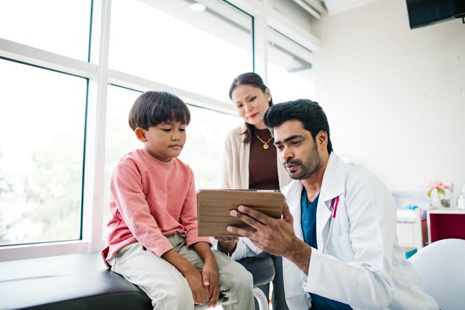 A Southeast Asian doctor showing a young boy a video during an appointment.