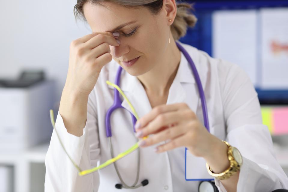 Tired doctor with glasses in hand holding his eyes in clinic
