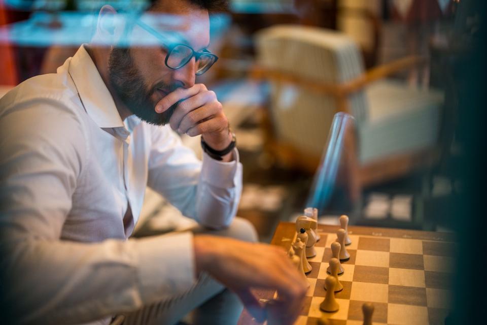 Focused Latin Man Engages in Chess Game at Boutique Hotel Lounge