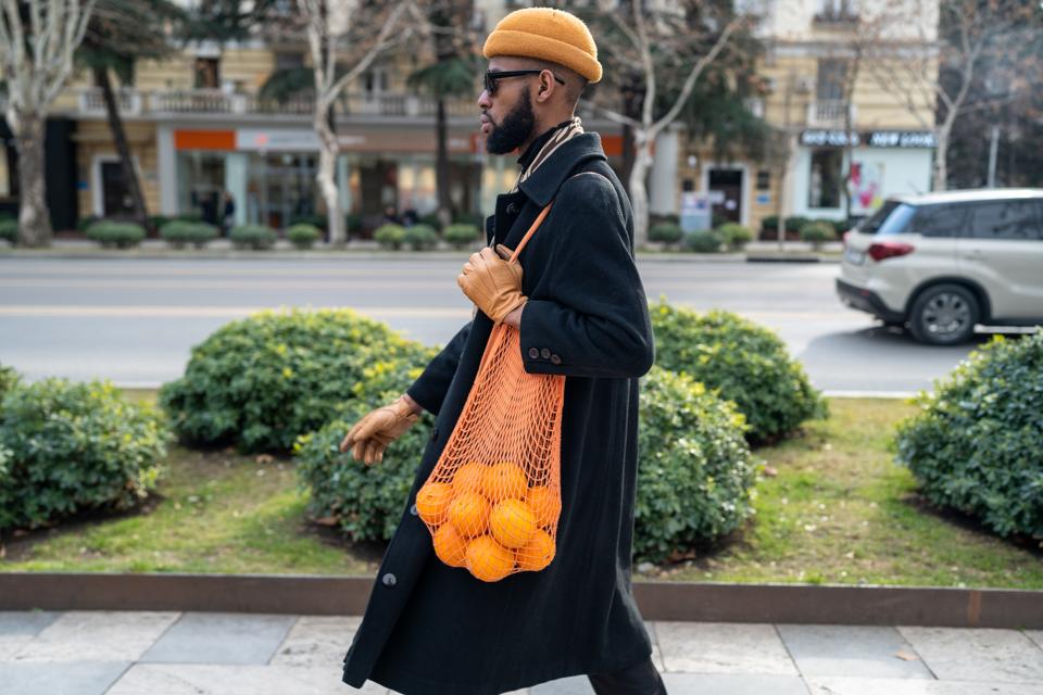 African American walking city street carrying oranges in reusable cotton mesh shopping bag
