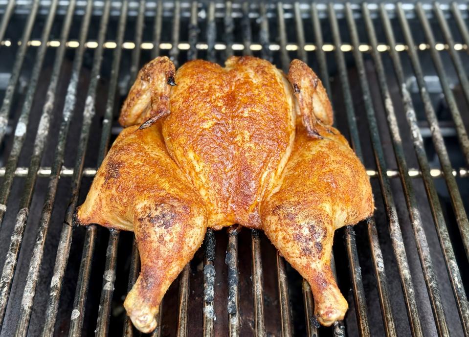The sweet, smoky, spicy blend of dry spices turn an ordinary chicken into an extraordinary meal. This photograph taken by Elizabeth Karmel of Smoky Honey Habanero Chicken on the grill shows a butterflied chicken with a nice burnished brown red glaze on the grilled chicken.