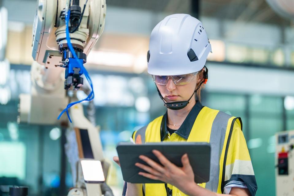 Female engineer in factory checking machinery status on laptop