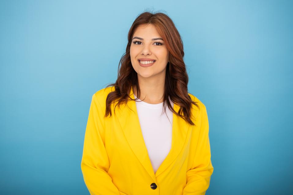 Confident latin leader in yellow jacket, beaming because she is delivering micro generosity