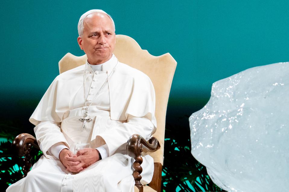 Pope Leo XIV sits in a chair on stage, a giant chunk of ice to his right