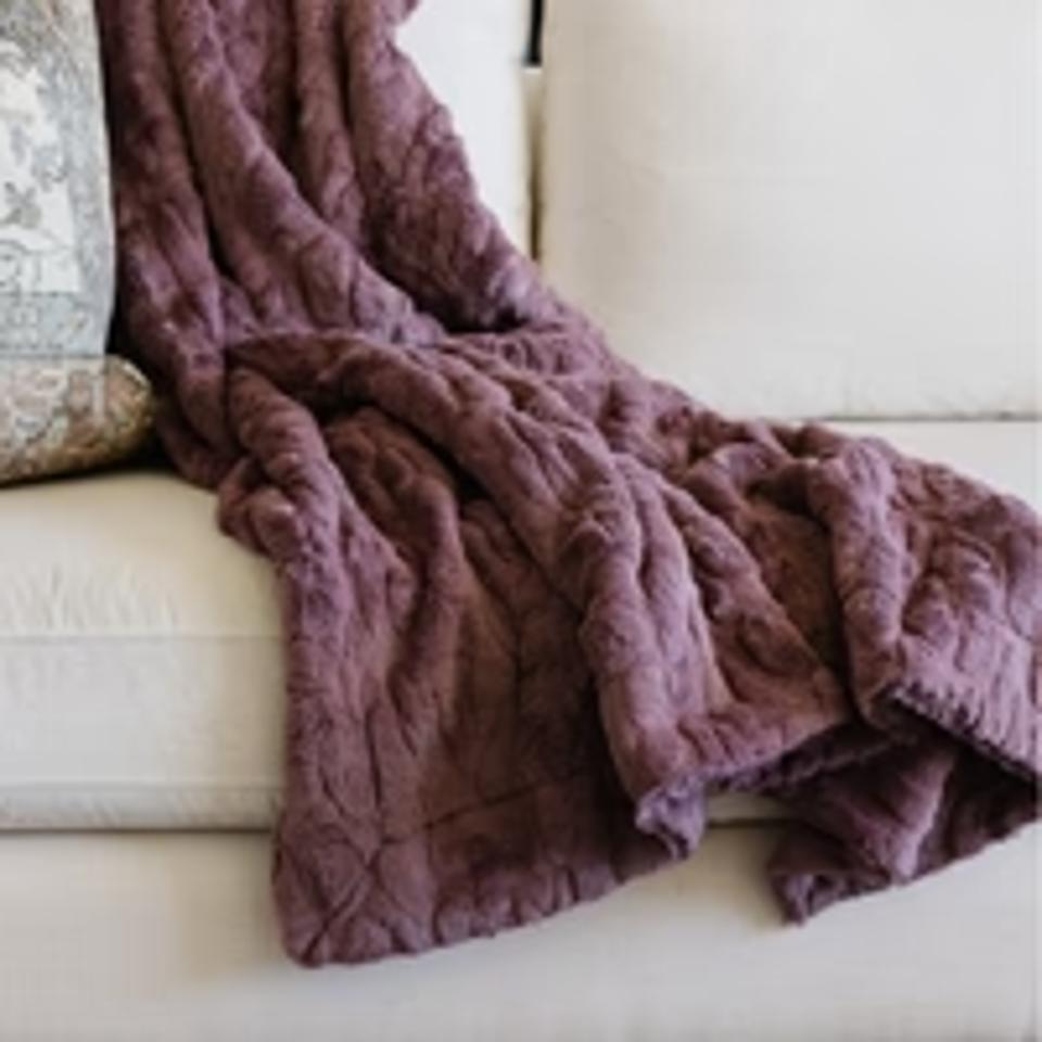 The Saranoni Faux Fur Throw Blanket in the color dusty mauve draped over a couch