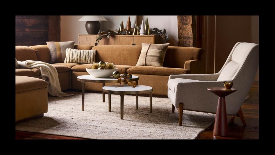 A cozy sectional couch with throw pillows and blankets, a nested coffee table and a Mid-Century modern-inspired chair.