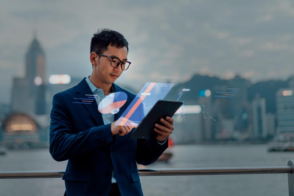 Young Asian businessman doing financial analysis with digital tablet against cityscape