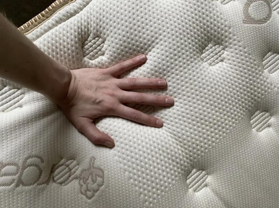 A hand feeling the top of the Saatva Classic Mattress.