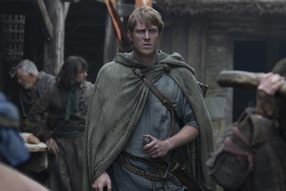 A man wearing a green cloak and holding a sword in a sheath