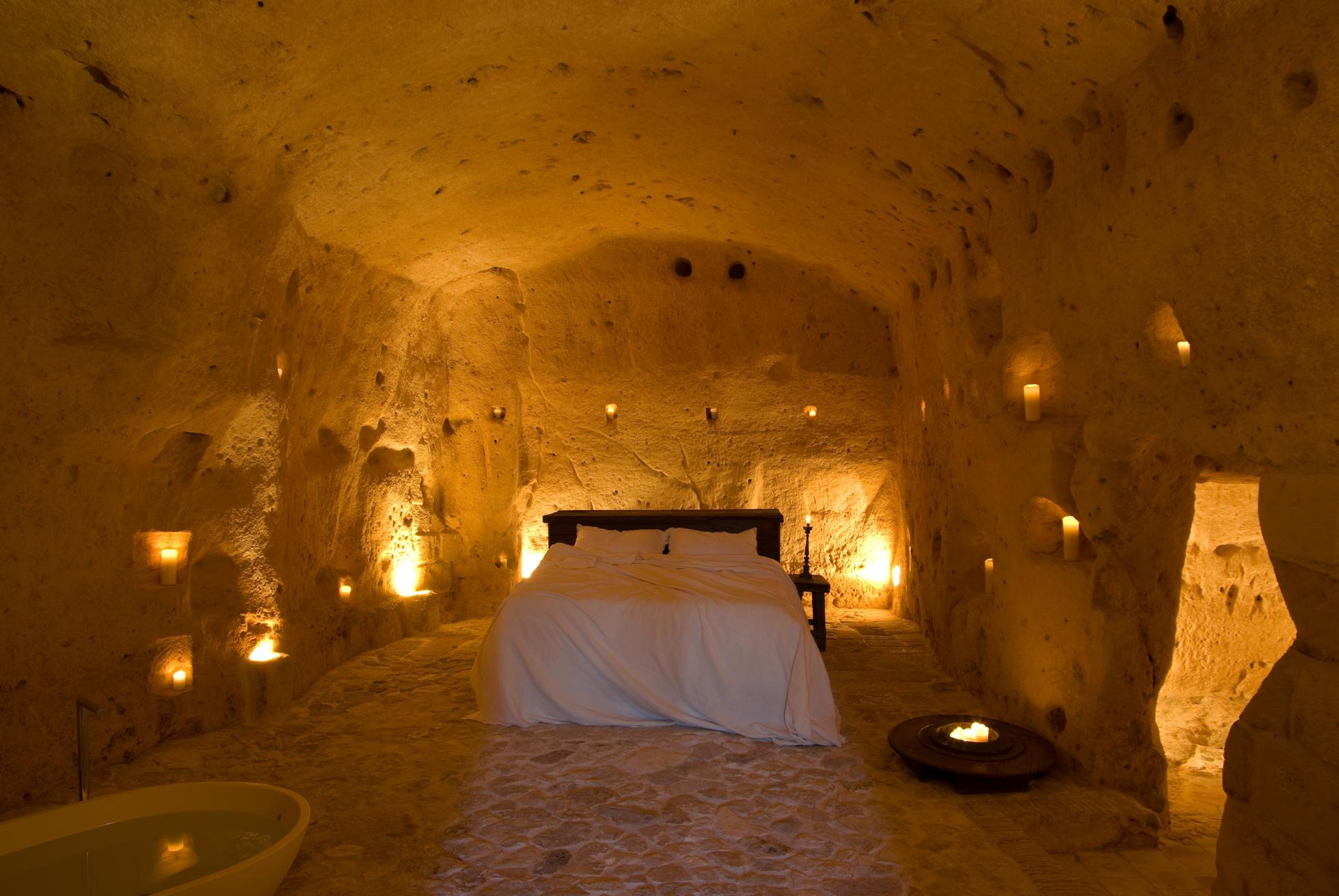 A fluffy white bed sits inside a lantern-lit cave at the Sextantio hotel in Matera, Italy