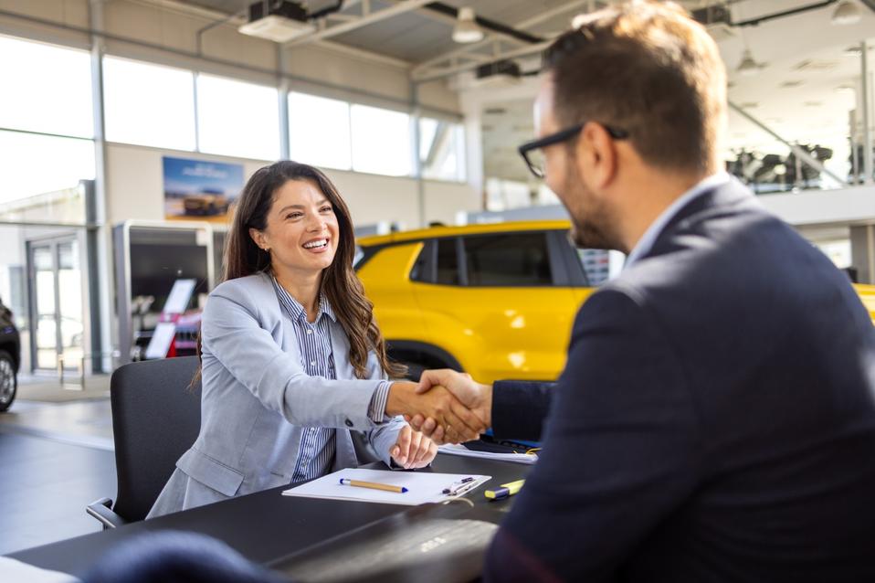 Beautiful woman Buying New Car Signing Papers With Dealer Man Standing In Auto Dealership Store.