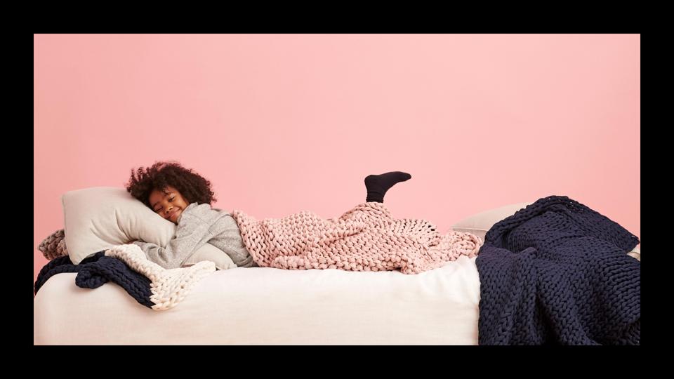 Young girl lying on a bed, covered in a weighted blanket