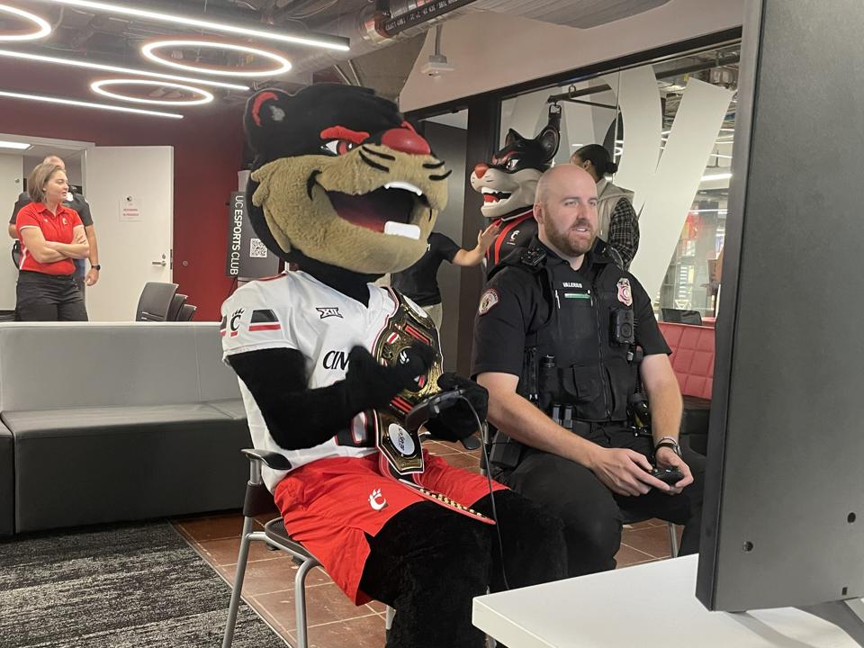 Bearcat mascot playing EA Sports College Football with a campus safety officer.