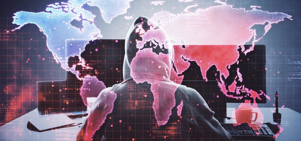 Hacker in hoodie using computer with digital world map overlay, cyber security.