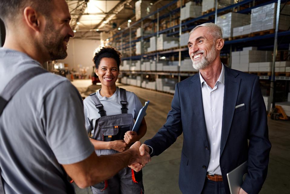 Manager and worker shaking hands next to colleague in distribution warehouse.