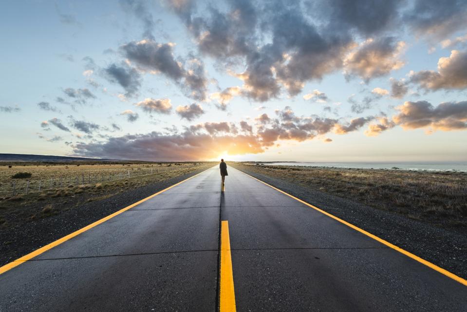 Person walking in the middle of the road towards sunset