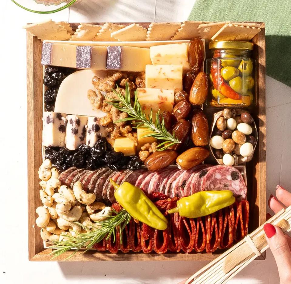 left hand holding boarderie cheese and charcuterie board w/ greenery in background daytime