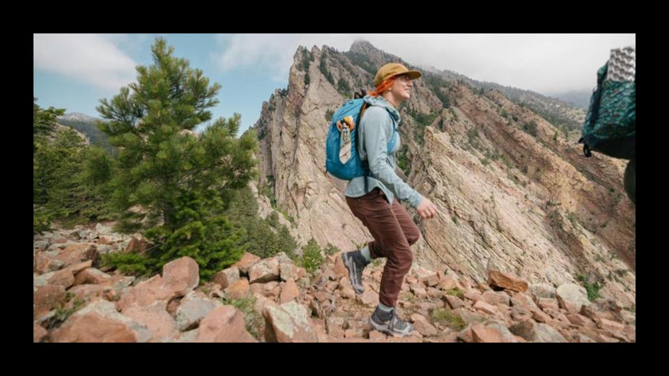 A woman hiking wearing a blue top and brown pants.